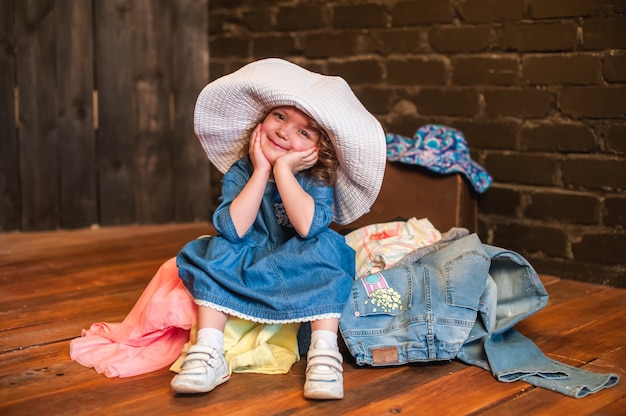 Foto menina de chapéu branco sentado na mala com as coisas e olhar para a câmera