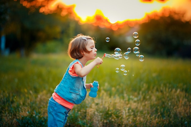 Menina de cinco anos de idade caucasiano criança soprando bolhas de sabão ao ar livre ao pôr do sol.