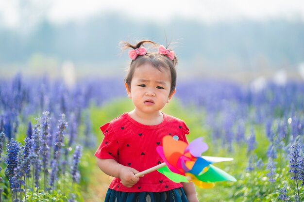 Menina de crianças em um jardim de flores segurando um moinho de vento de brinquedo, olhando para a câmera