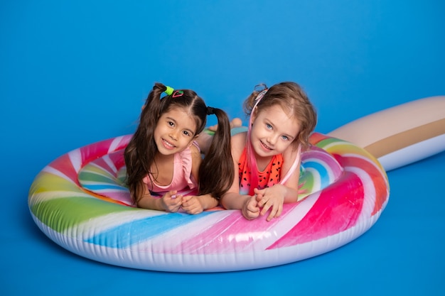 Menina de duas crianças felizes em fato de banho deitado no pirulito colorido colchão inflável.