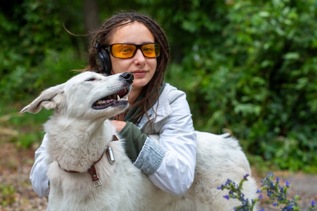 Menina de fones de ouvido e óculos abraça um cachorro.
