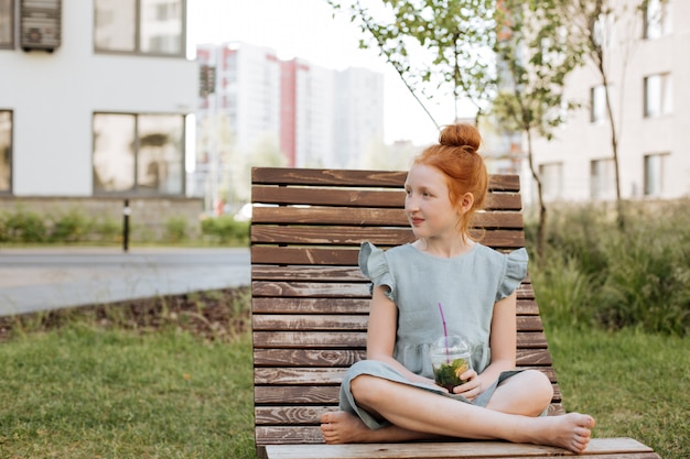 Menina de gengibre com limonada em um copo de plástico