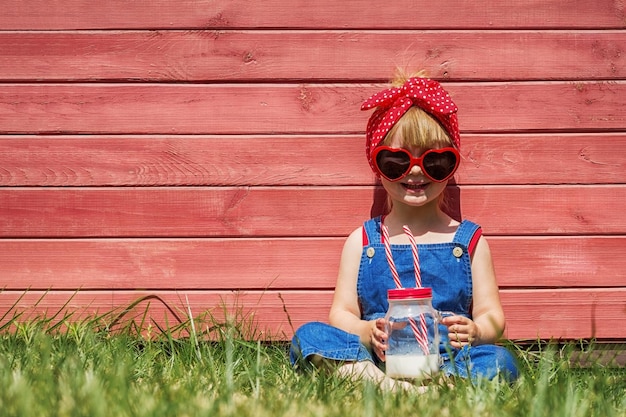 Menina de macacão e óculos de sol está bebendo leite Conceito de verão colorido Copiar espaço