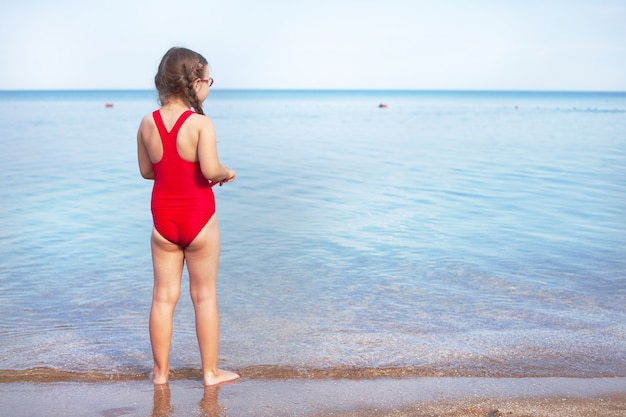 Menina de maiô vermelho e óculos brincando na praia