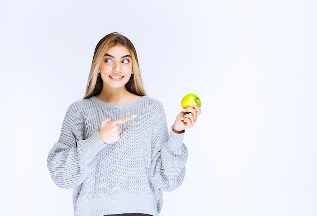 Menina de moletom cinza segurando a maçã verde na mão.