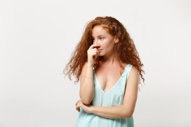 Menina de mulher jovem linda ruiva preocupada insatisfeita em roupas leves casuais posando isolado no fundo branco. Conceito de estilo de vida de pessoas. Simule o espaço da cópia. Olhando para o lado, colocando a mão no nariz.