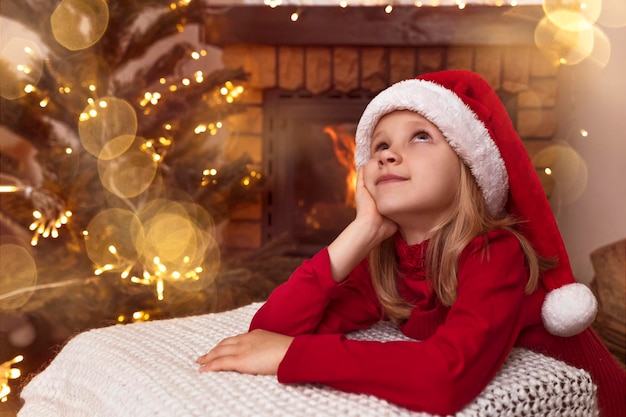 Menina de Natal com chapéu vermelho de Papai Noel sonhando e esperando o Papai Noel na casa de Natal