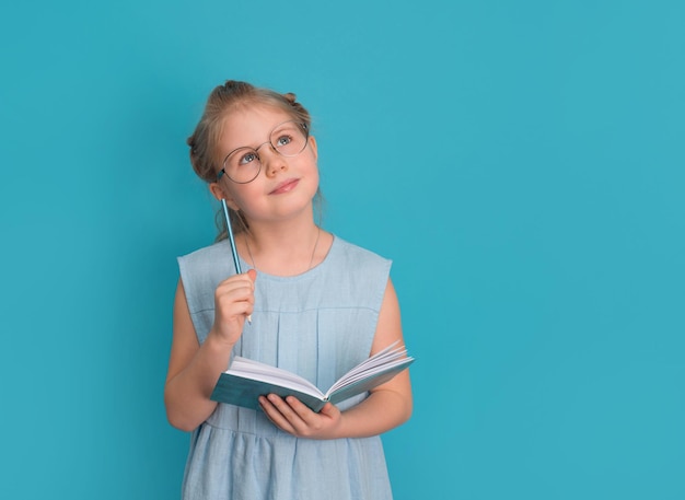 Menina de óculos com caderno ou diário e lápis sobre fundo azul