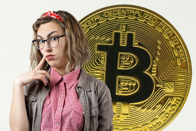 Menina de óculos e uma camisa no fundo do Bitcoin. Pensando na pergunta, expressão pensativa