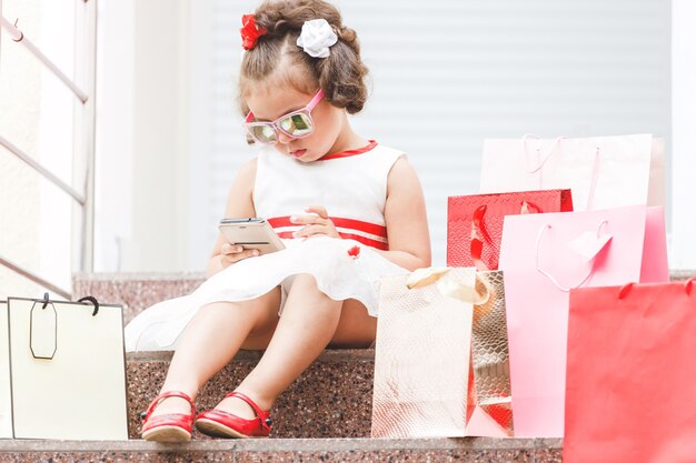 Menina de óculos escuros sentada na escadaria do shopping com sacolas coloridas