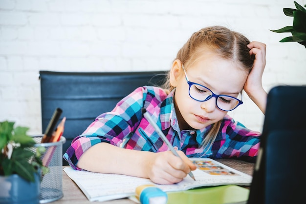 Menina de óculos estudando online em casa uma menina da escola primária com computador com zoom vi...