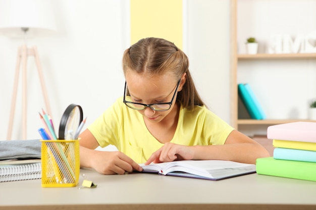 Menina de óculos lendo um livro em casa