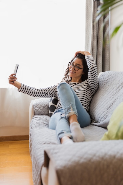 Menina de óculos sentada na sala de estar tirando uma selfie com o telefone