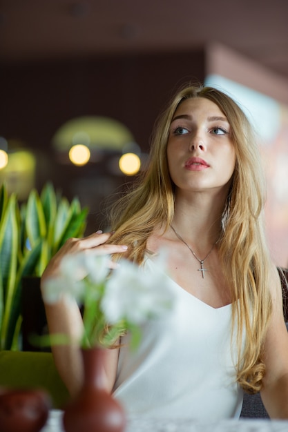 Menina de olhos azuis, sentada no café urbano. mulher com penteado ondulado marrom. Conceito de estilo de vida.