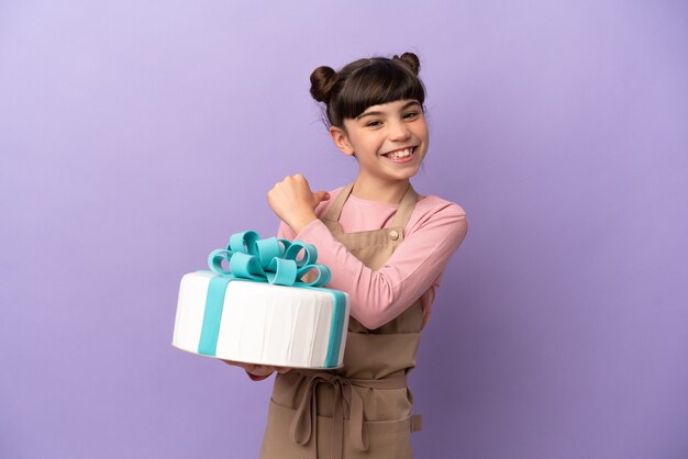 Menina de pastelaria segurando um grande bolo isolado em um fundo roxo orgulhosa e satisfeita