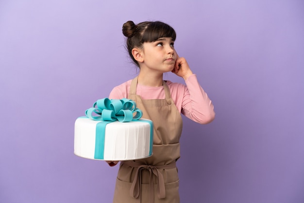 Menina de pastelaria segurando um grande bolo isolado na parede roxa, tendo dúvidas e pensando