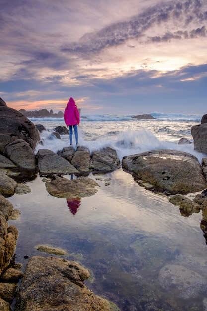 Menina de pé em uma pedra e olhando para o mar no pôr do sol