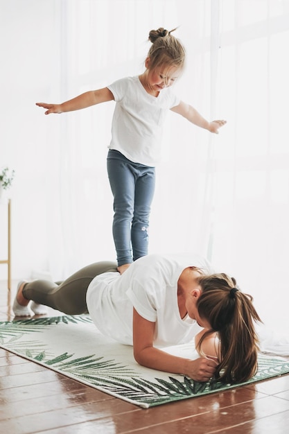 Menina de pé nas costas da mãe a fazer exercícios em casa