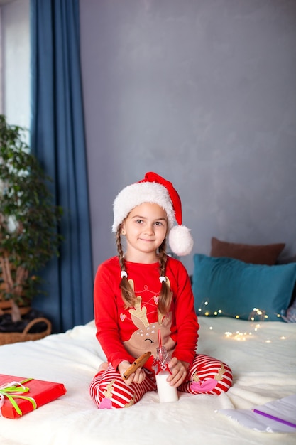 menina de pijama sentada com leite e biscoitos de Natal