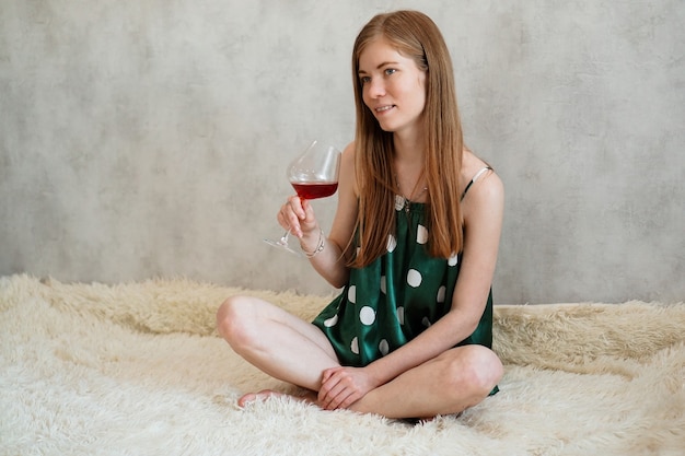 Menina de pijama verde na cama com uma taça de vinho tinto