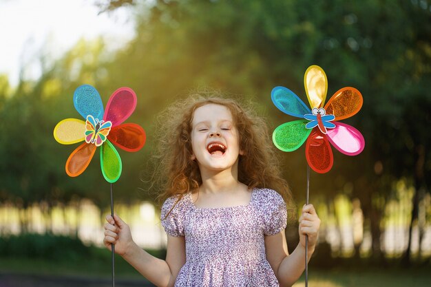 Menina de riso que guarda brinquedos de um pinwheel do arco-íris.