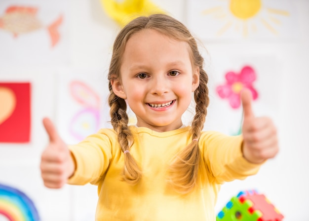 Menina de sorriso bonita no pulôver amarelo que faz os polegares acima.