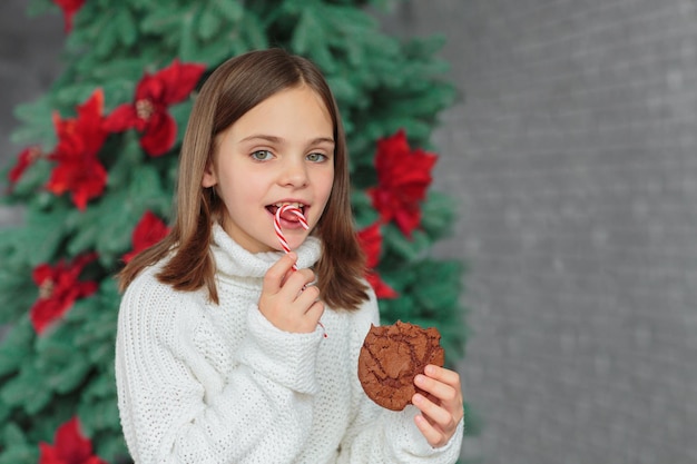 Foto menina de suéter de malha branca sorrindo e comendo biscoito de natal