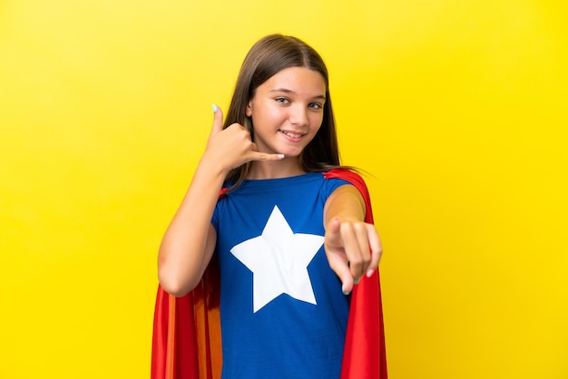 Menina de super-herói caucasiana isolada em fundo amarelo fazendo gesto de telefone e apontando para a frente
