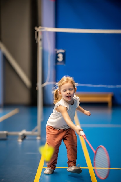 Menina de três anos jogando badminton em roupas esportivas na quadra coberta