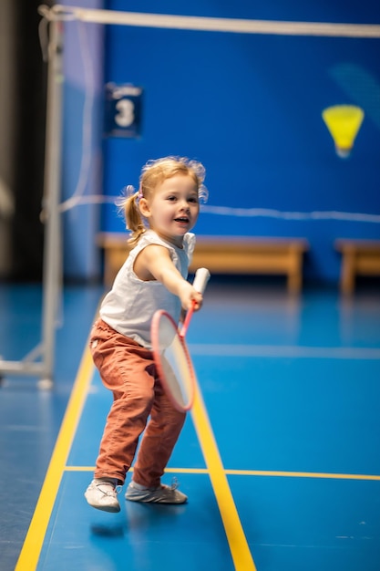 Menina de três anos jogando badminton em roupas esportivas na quadra coberta