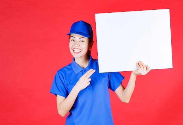 Menina de uniforme azul e boina, segurando uma mesa de informações quadrada branca e se sentindo positiva.