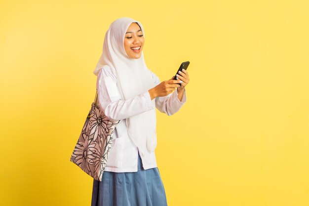 Foto menina de uniforme de ensino médio com véu feliz enquanto usa telefone celular em fundo isolado