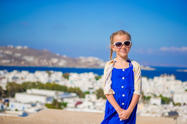 Menina de vestido azul ao ar livre. garoto na rua da típica vila tradicional grega, com paredes brancas e portas coloridas na ilha de mykonos, na grécia