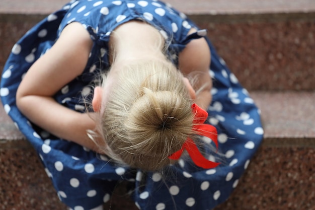 Menina de vestido azul sentada na escada e chorando