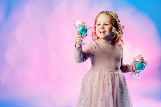Foto menina de vestido bege tem 2 bolas de sorvete nas mãos dela sobre um fundo azul e sorri