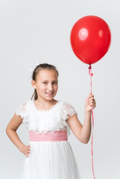 Menina de vestido branco segurando balões de ar vermelho na mão feliz sorrindo olhando para a câmera Vista frontal