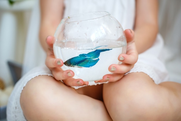 Menina de vestido branco segurando um aquário com peixes azuis.