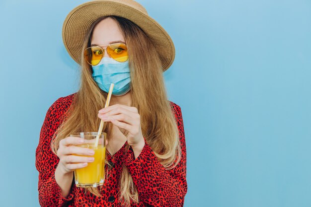 Menina de vestido, chapéu e óculos de sol com uma máscara médica na cara dela.