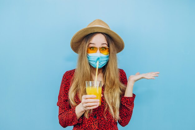 Menina de vestido, chapéu e óculos de sol com uma máscara médica na cara dela.
