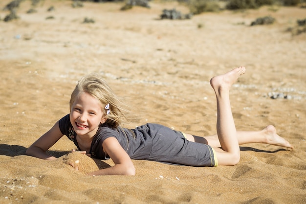 Menina de vestido cinza está descansando na areia quente.