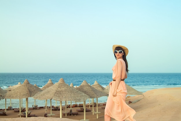 Menina de vestido com óculos posando perto da praia do mar