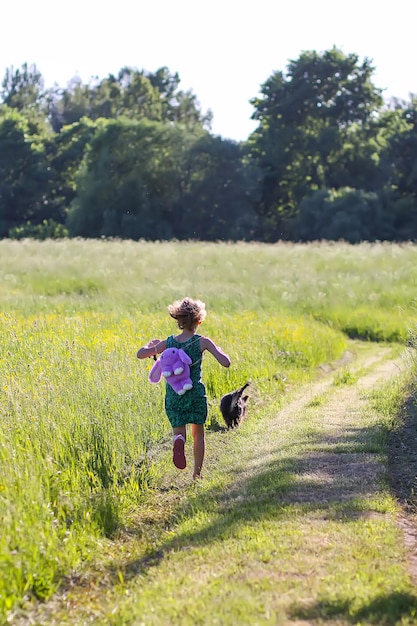 Menina de vestido de verão com mochila andando com pequeno cachorro preto na trilha no campo verde de verão