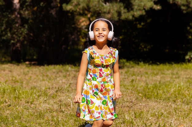 Menina de vestido e fones de ouvido está se divertindo e pulando no parque na grama.