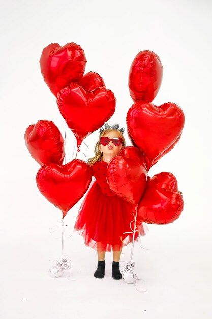Menina de vestido e óculos de sol em forma de coração esconde-se entre balões e beijos
