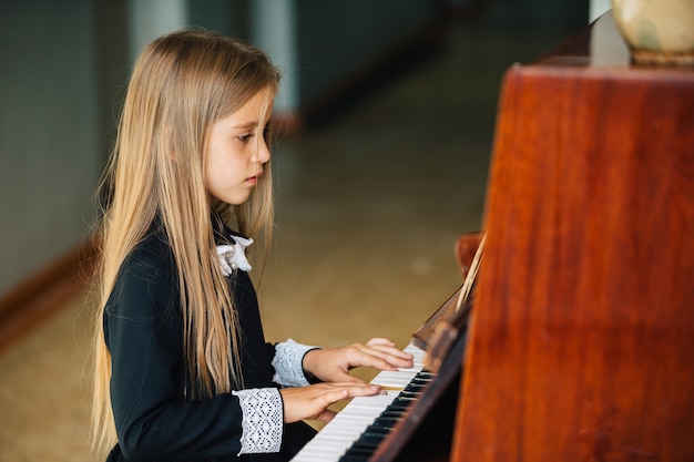 Menina de vestido preto aprende a tocar piano. a criança toca um instrumento musical.