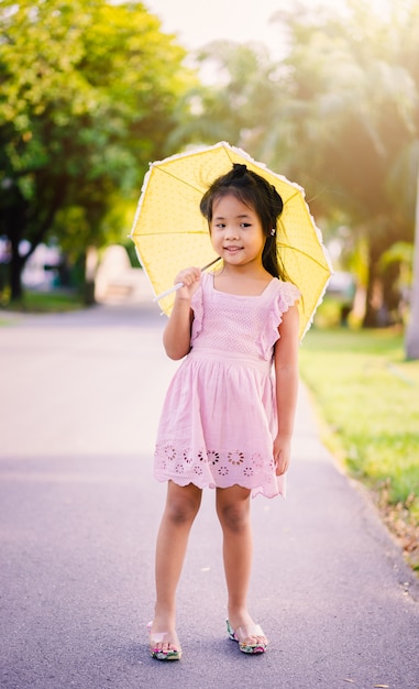 Menina de vestido rosa com guarda-chuva amarelo em dia de sol