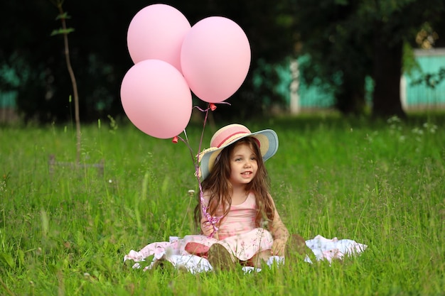 Menina de vestido rosa com um chapéu, senta-se na grama do parque. Foto de alta qualidade