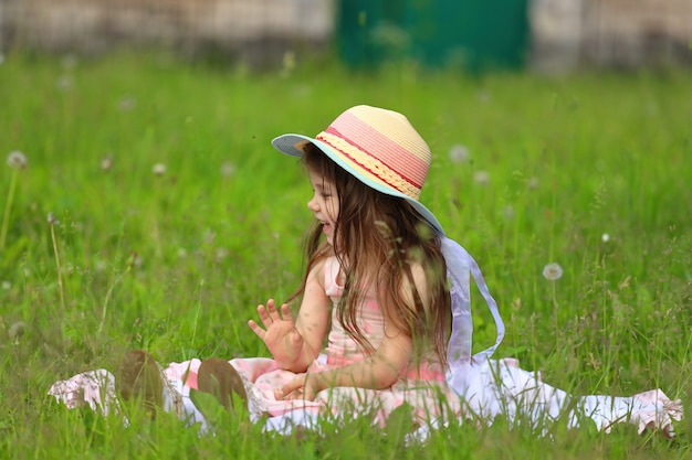 Menina de vestido rosa com um chapéu, senta-se na grama do parque. Foto de alta qualidade