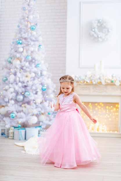 Menina de vestido rosa perto da árvore de Natal