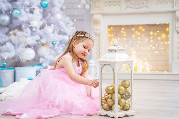 Menina de vestido rosa perto da árvore de Natal